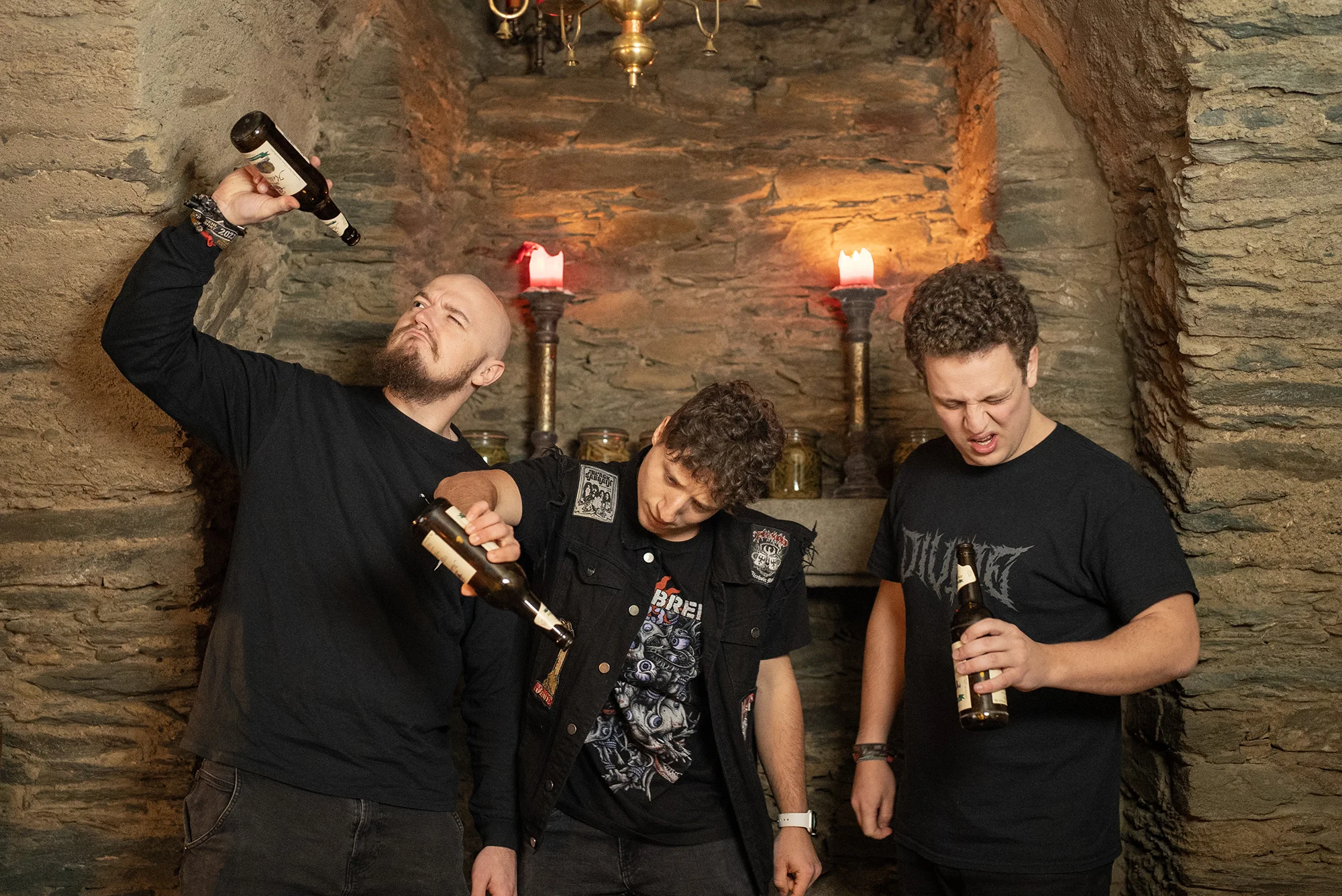 Band photo from Chronic Thirst.
Three men, dressed in black, stand in front of a light brick wall. Two candlesticks stand on a ledge, you can see a chandelier above.
Everyone has beer bottles in their hands and is visibly upset that they are empty.