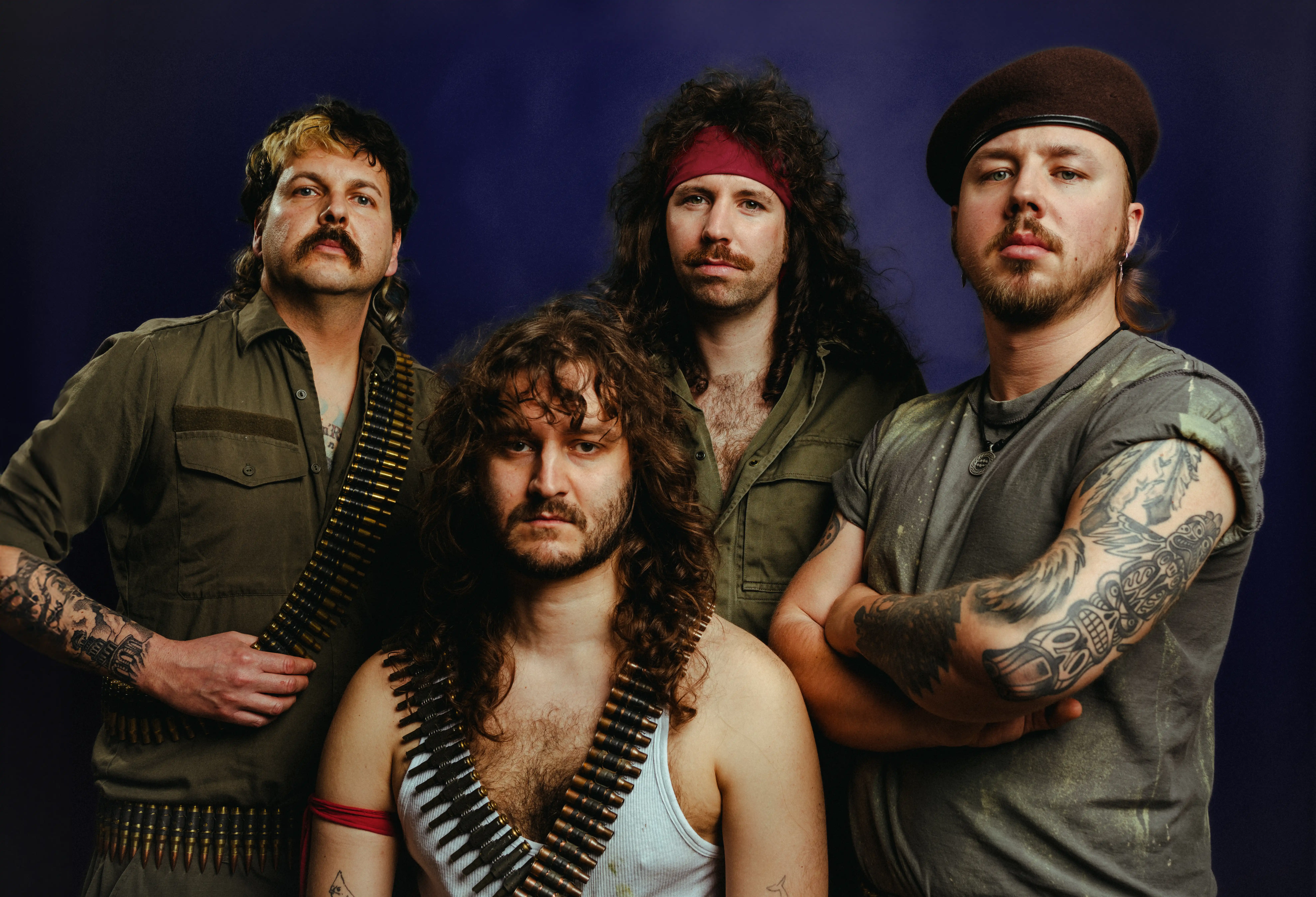 Mechanic Tyrants Bandfoto.
Vier Männer mit langen Haaren. Einer trägt ein rotes Bandana, einer ein Barett in braun.
Die drei hinteren sind in Militär-grün gekleidet. Der vordere trägt eine weißes Tanktop und ein rotes Band um den Oberarm.
Zwei tragen je zwei Patronengürtel.
Sie schauen neutral in die Kamera.