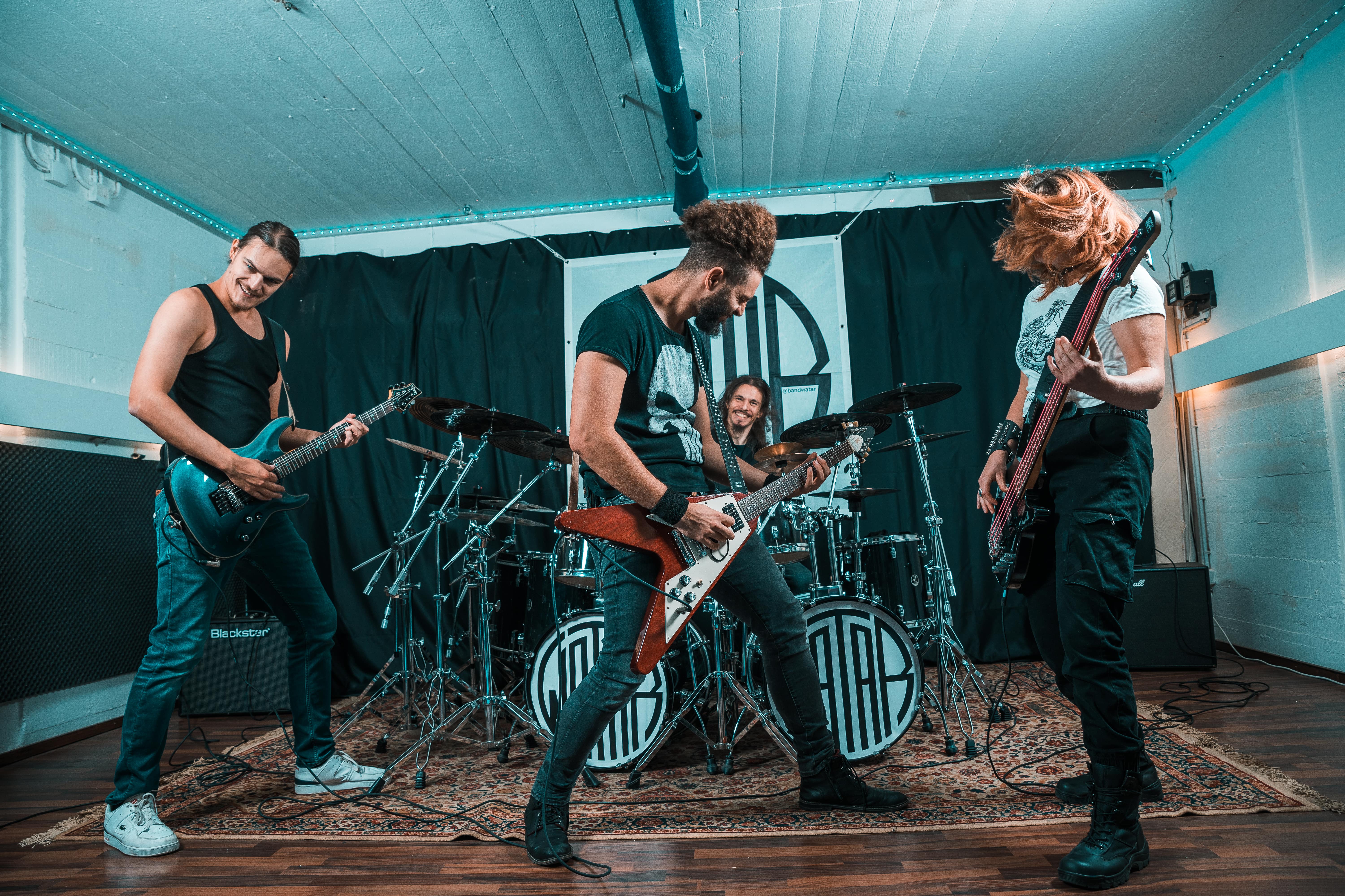 Bandphoto of Watar in their rehearsal room in action.
Two men playing guitar, one man at the drums and one woman playing bass.